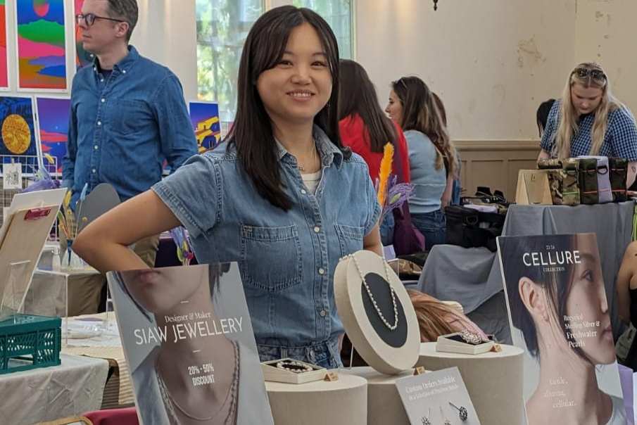 Woman standing behind a table displaying jewelry at an event with 'SIAW Jewellery' and 'CELLURE' branding.