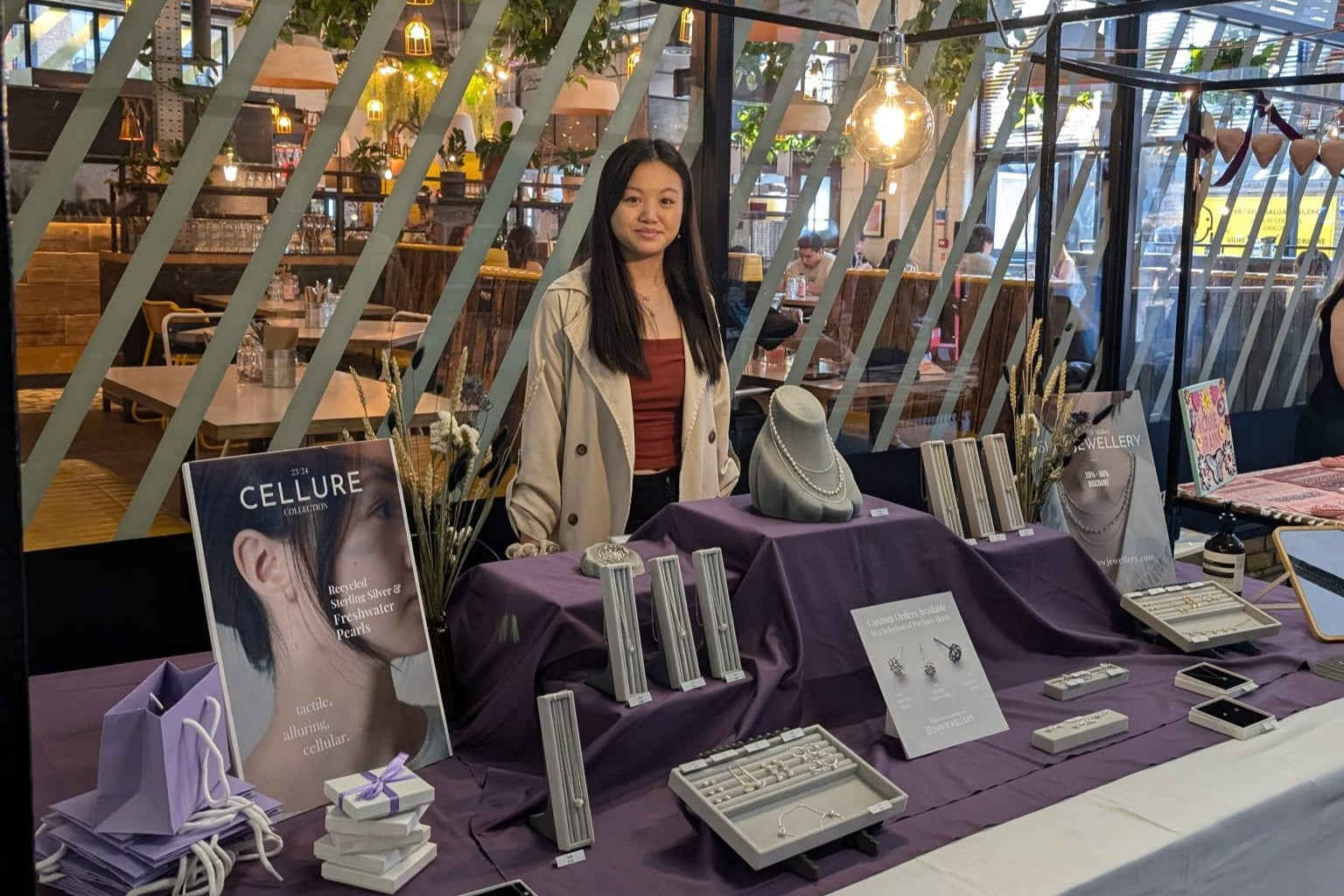 Woman standing behind a table with products and a magazine at an event.