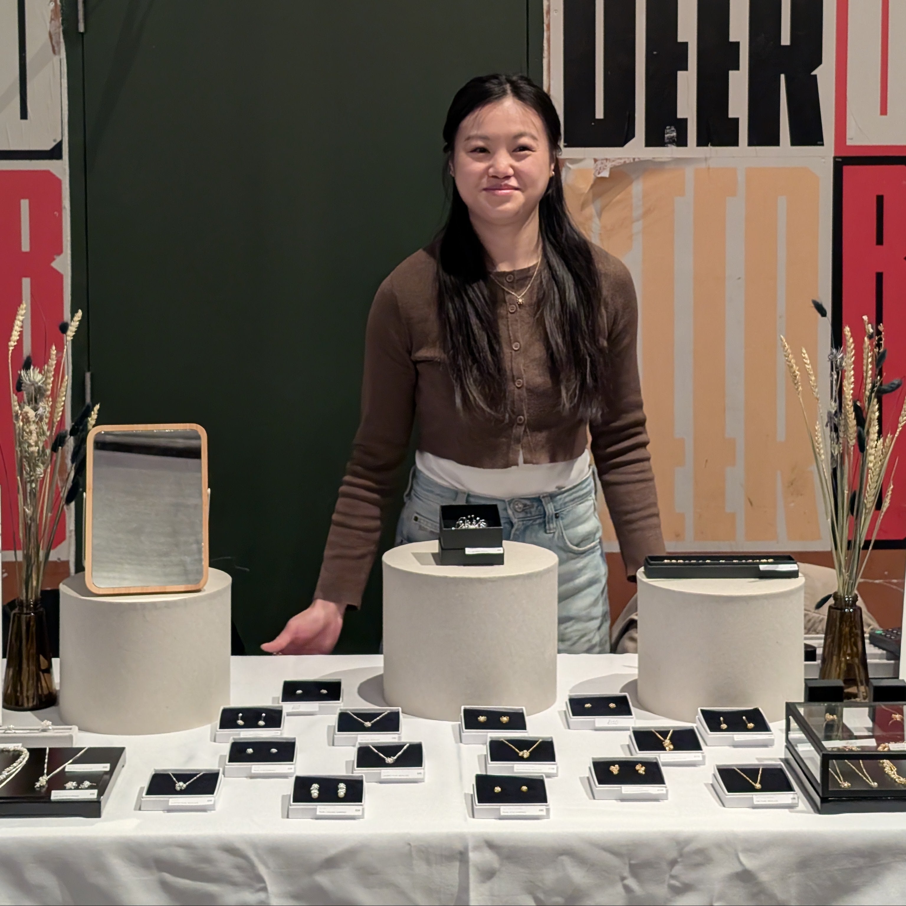 Person standing behind a table with products against a colorful 'BEER' backdrop